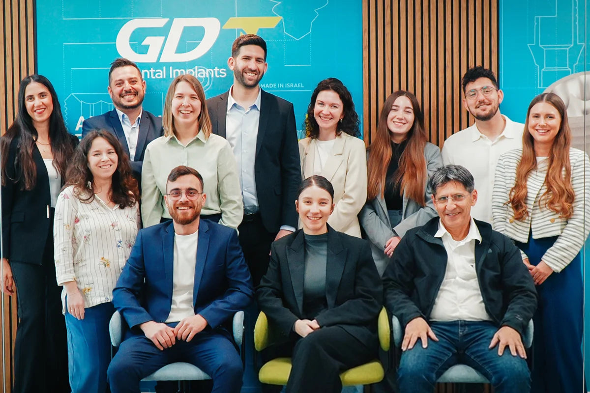 GDT Dental Implants team group photo in the office lobby, with the GDT logo backdrop and staff seated and standing.