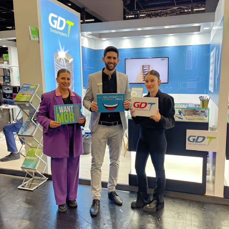 GDT Dental Implants representatives holding branded signs at the IDS 2023 booth in Cologne, Germany.