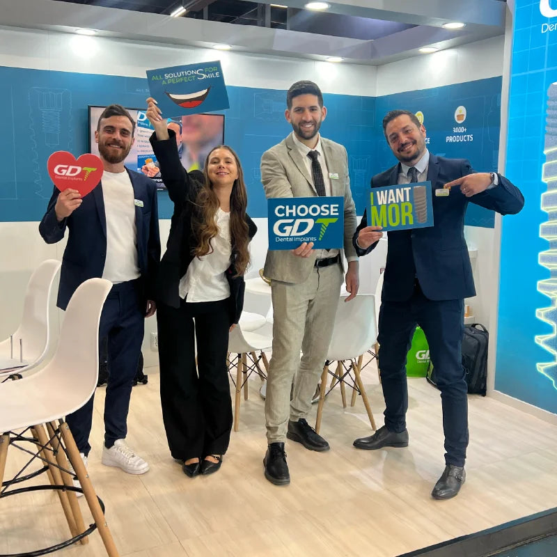 GDT Dental Implants team holding branded signs at the IDS 2025 exhibition booth in Cologne, Germany.