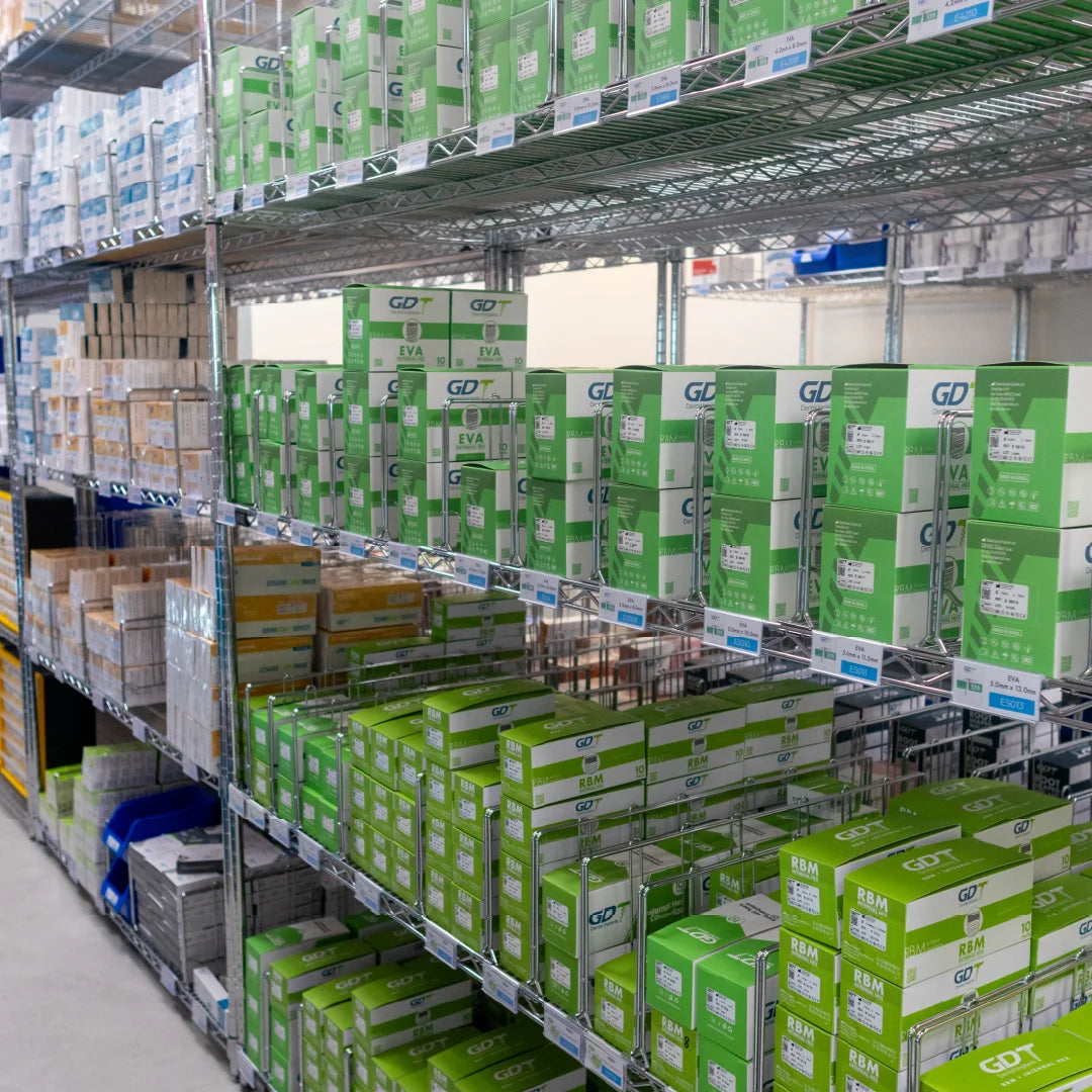 warehouse shelving stocked with many green and white boxes, including repeated GDT and EVA branding, in a bright industrial storage aisle.