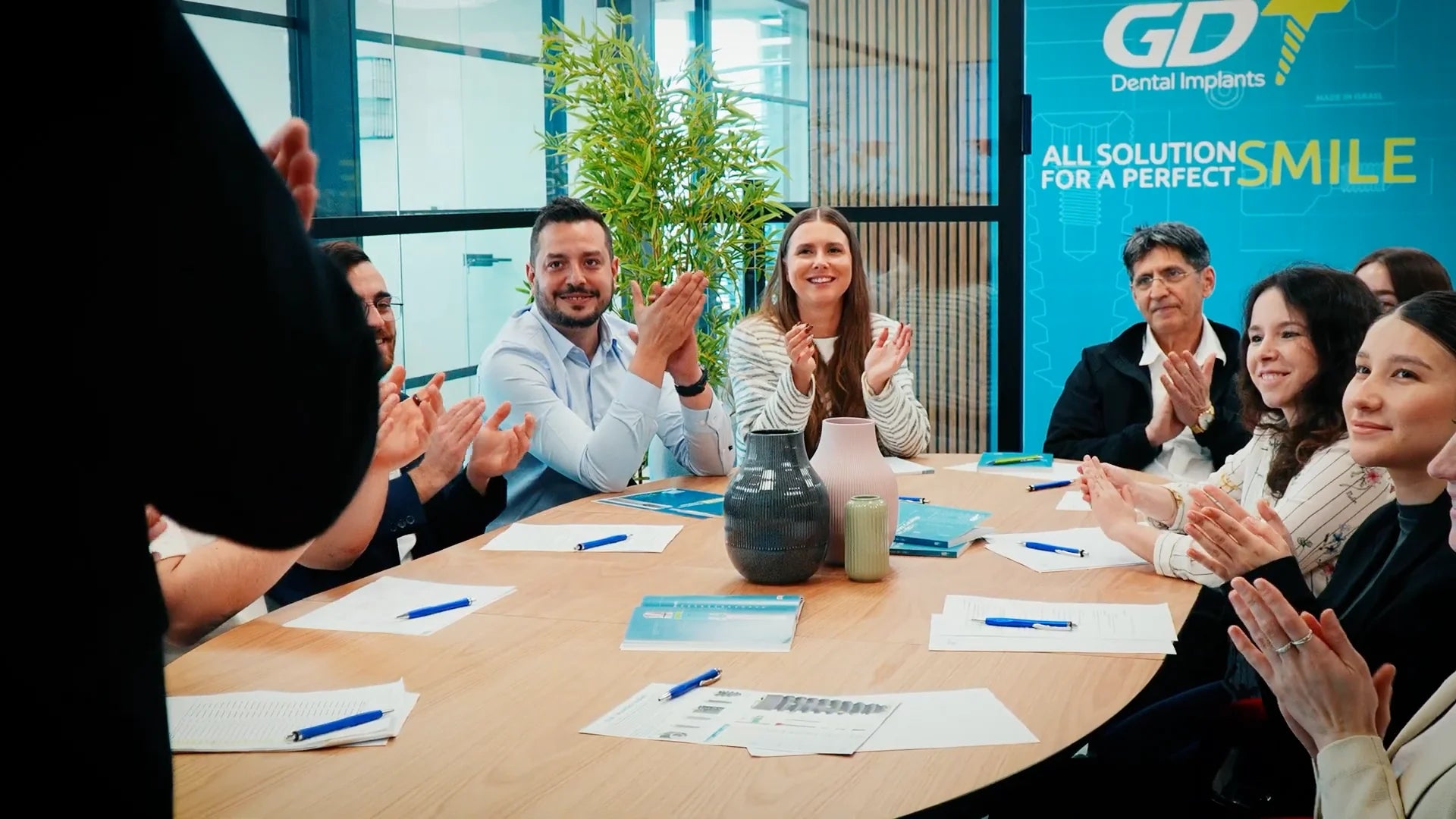 GDT Dental Implants team members applauding during a company meeting in a modern office conference room.
