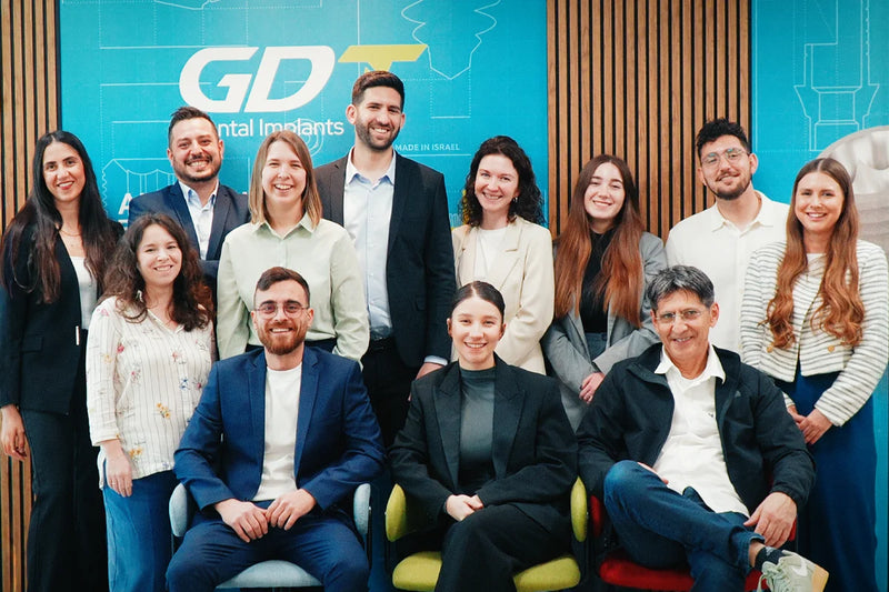 GDT Dental Implants team smiling together in front of company branding wall inside headquarters in Israel.
