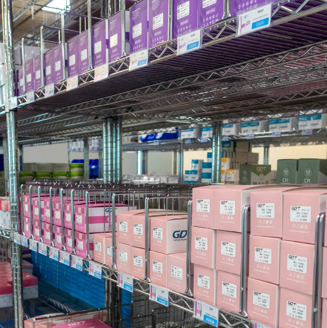 Shelves stocked with pink and purple GDT Implants boxes in a warehouse-like retail environment. 